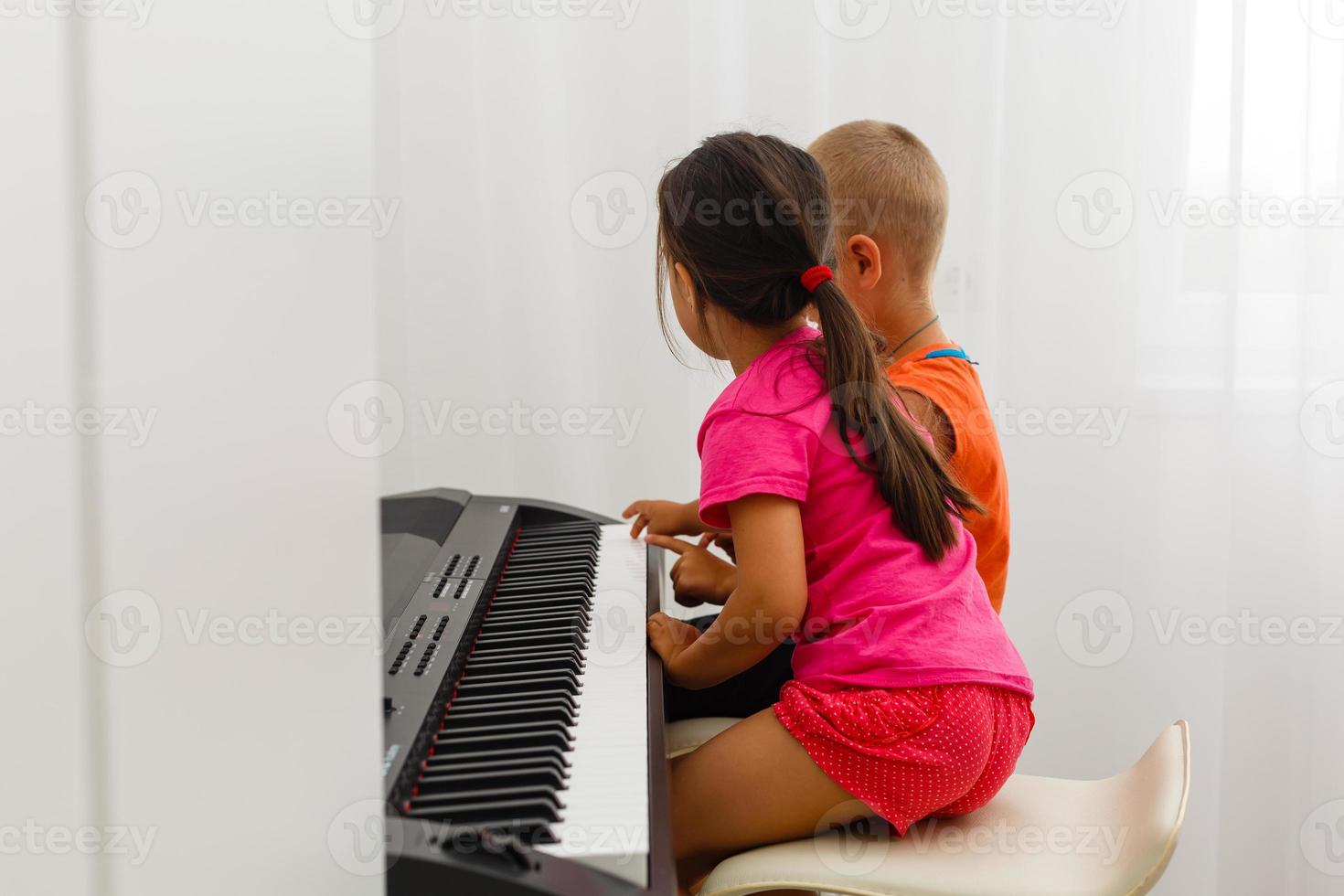 Two little kids girl and boy playing piano in living room or music school. Preschool children having fun with learning to play music instrument. Education, skills concept. photo