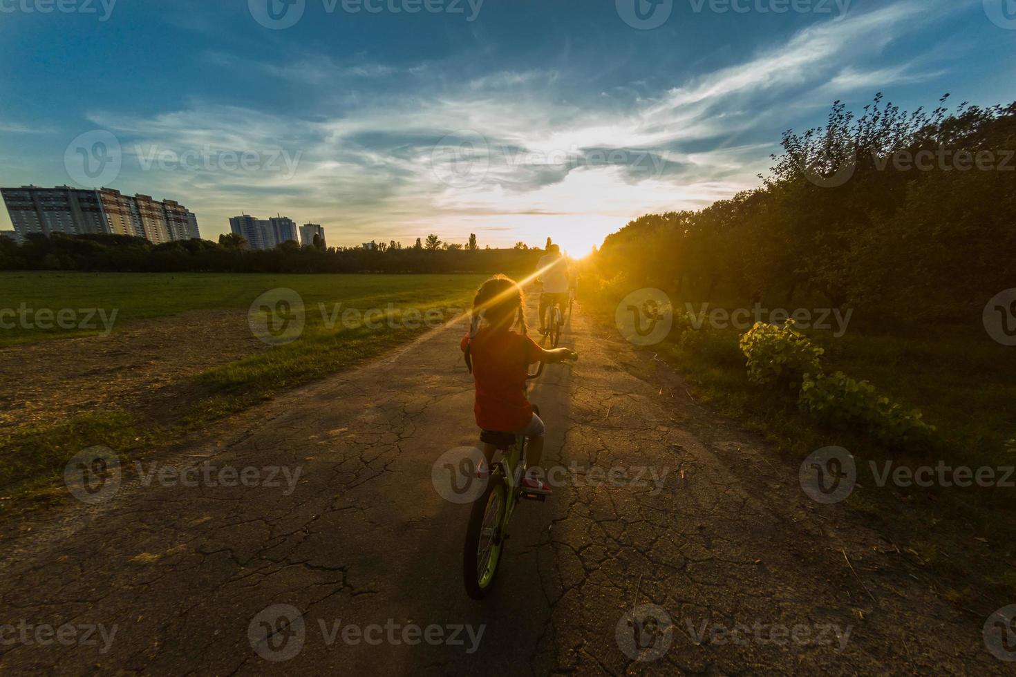 familia de Tres personas teniendo paseo en rural paisaje. hijo, madre y padre montando bicicletas terminado puesta de sol cielo antecedentes. familia ciclistas teniendo divertido en vacaciones foto