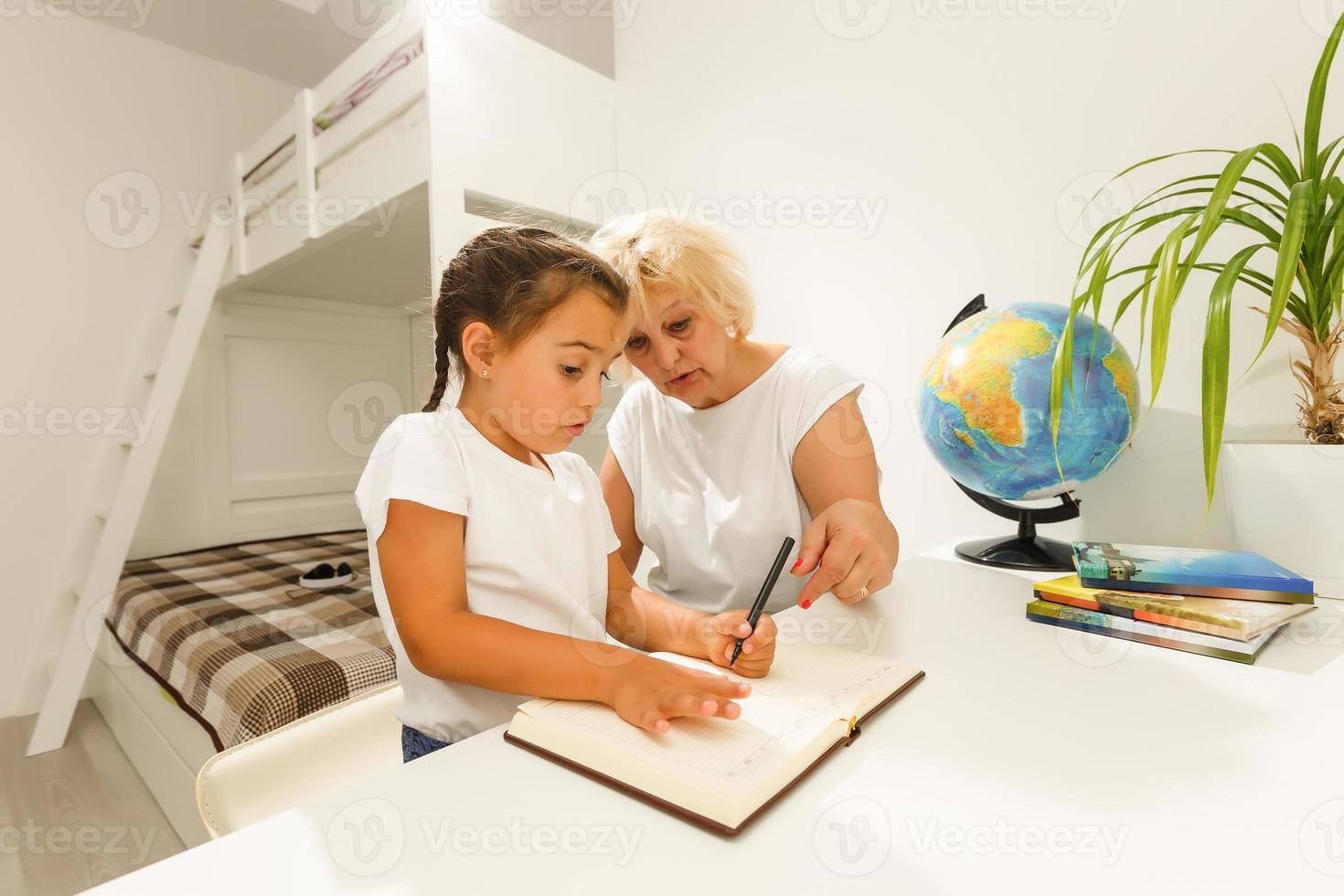 Grandmother help granddaughter doing school homework together at home photo