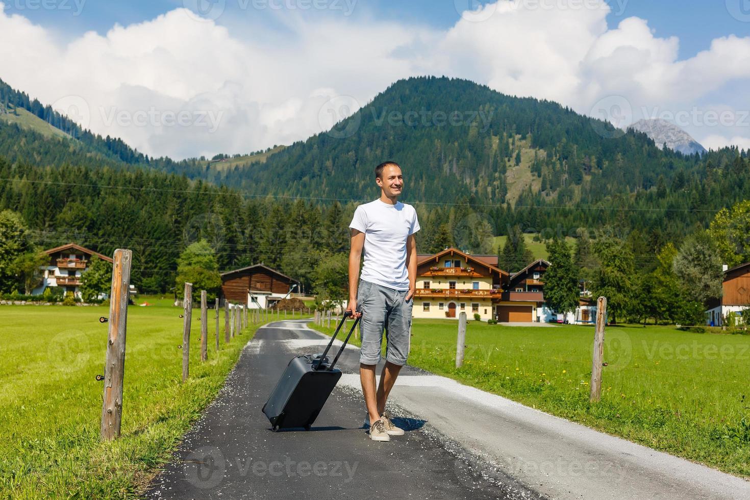 Traveler man walking with suitcase in the street in the mountains. Travel concept. photo