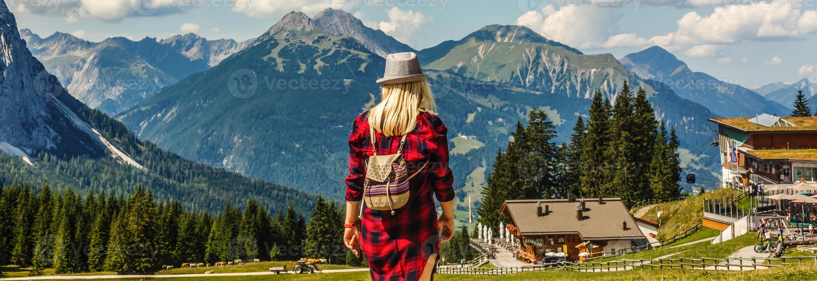 back view of blonde girl in hat with backpack standing near lake with sunlight photo