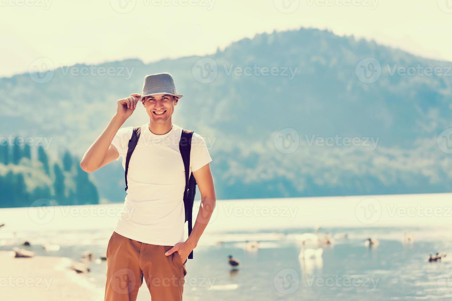 Handsome man over green nature and blue lake standing . Adventure, travel, tourism and leisure concept - young boy relaxing photo