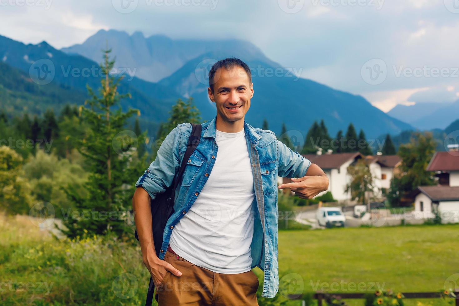 happiness, advertisement, fashion, gesture and people concept - smiling man in t-shirt pointing finger on himself in the mountains background photo
