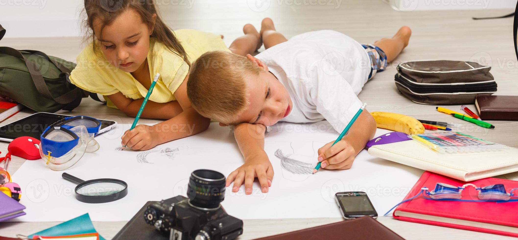 Cute children drawing lying on the floor with their parents in the background photo