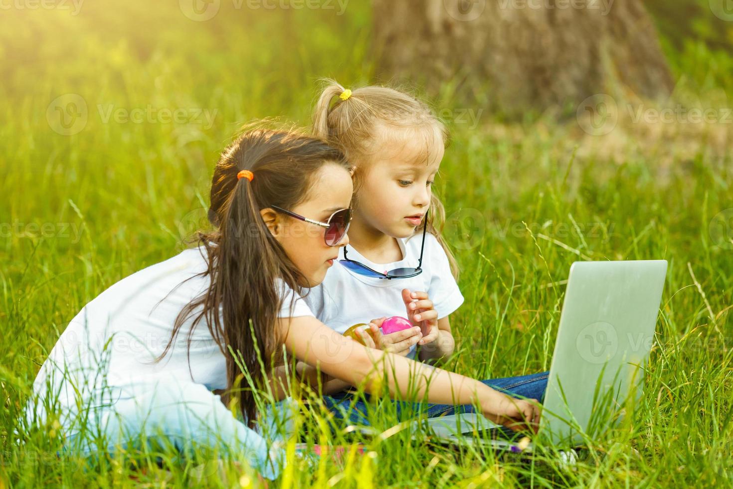 Two kids playing Laptop or Notebook in the garden for education. The concept is smart learning from internet and social media photo