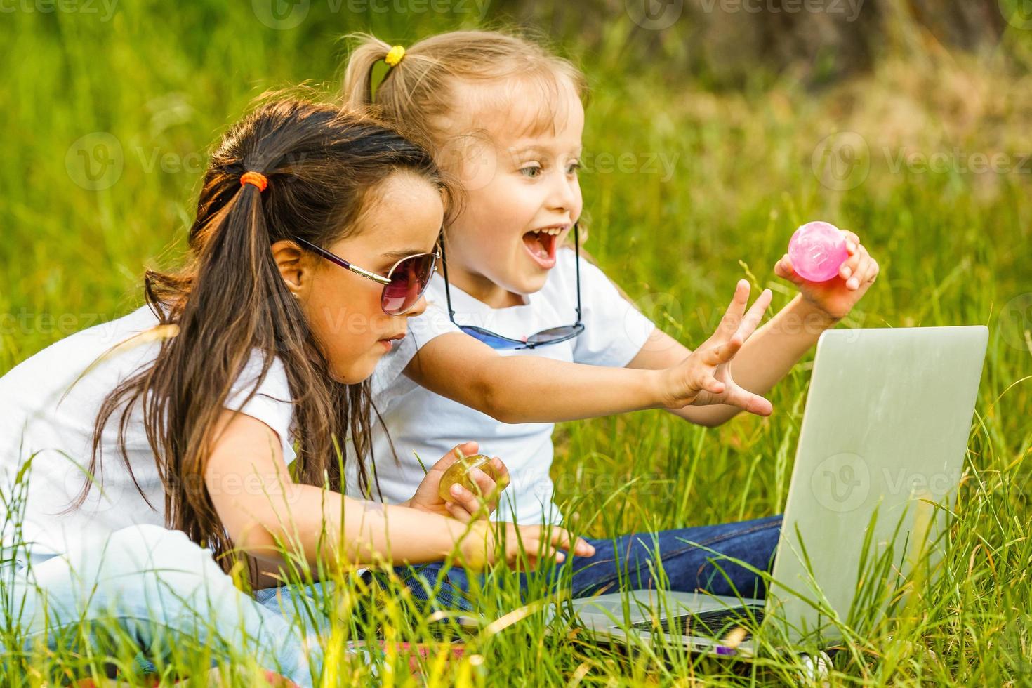 Two children sit in park under a big tree and play on the tablet. girl are keen on game. Him it is very cheerful photo