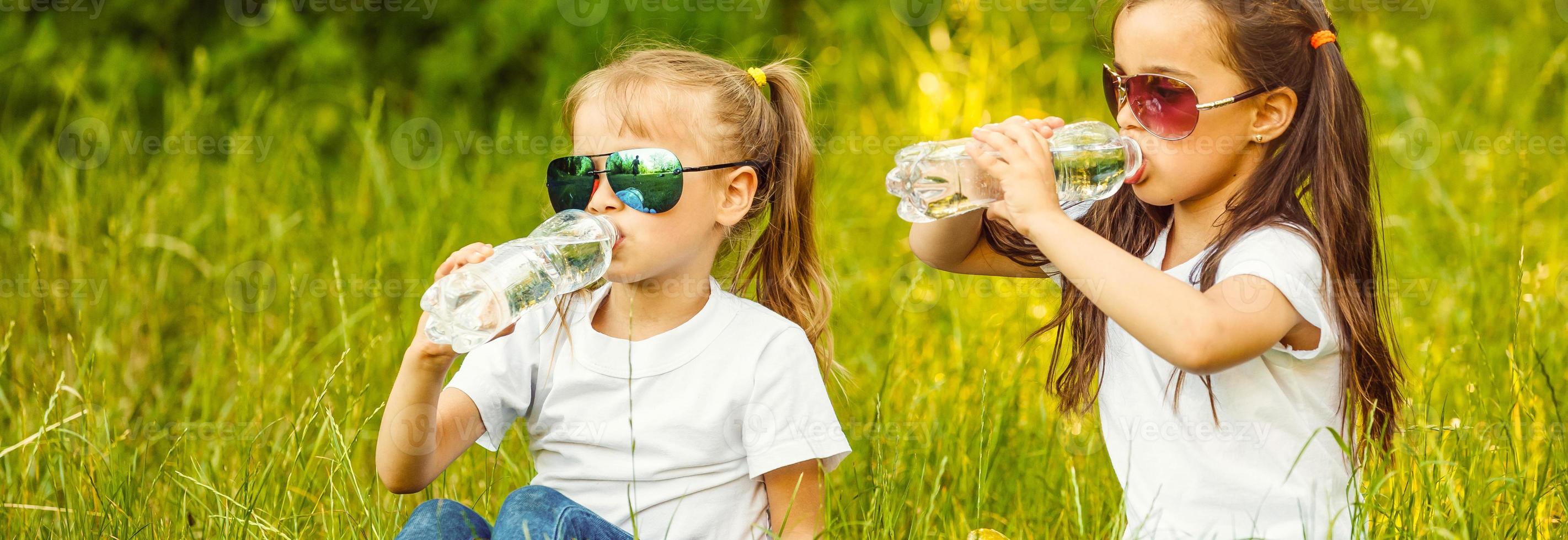 Small children refreshing themselves with water in the park. Little girl drinking water form a bottle in the city. photo