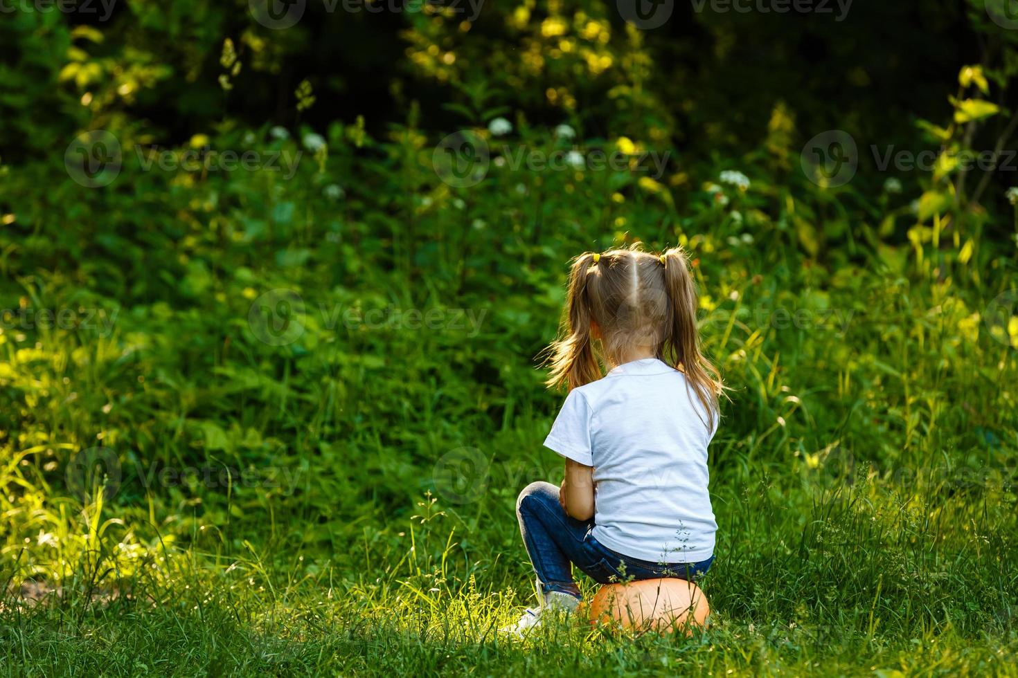 The smiling little cute baby girl is playing with small soccer ball for children on green grass playing field photo