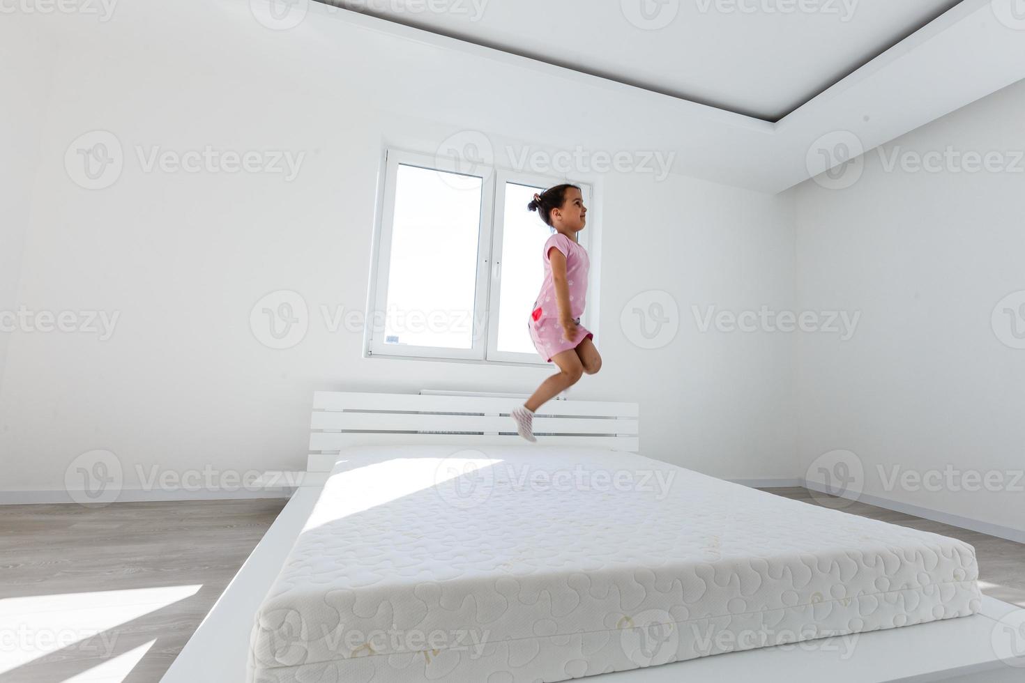 Cute little girl jumping on white bed photo