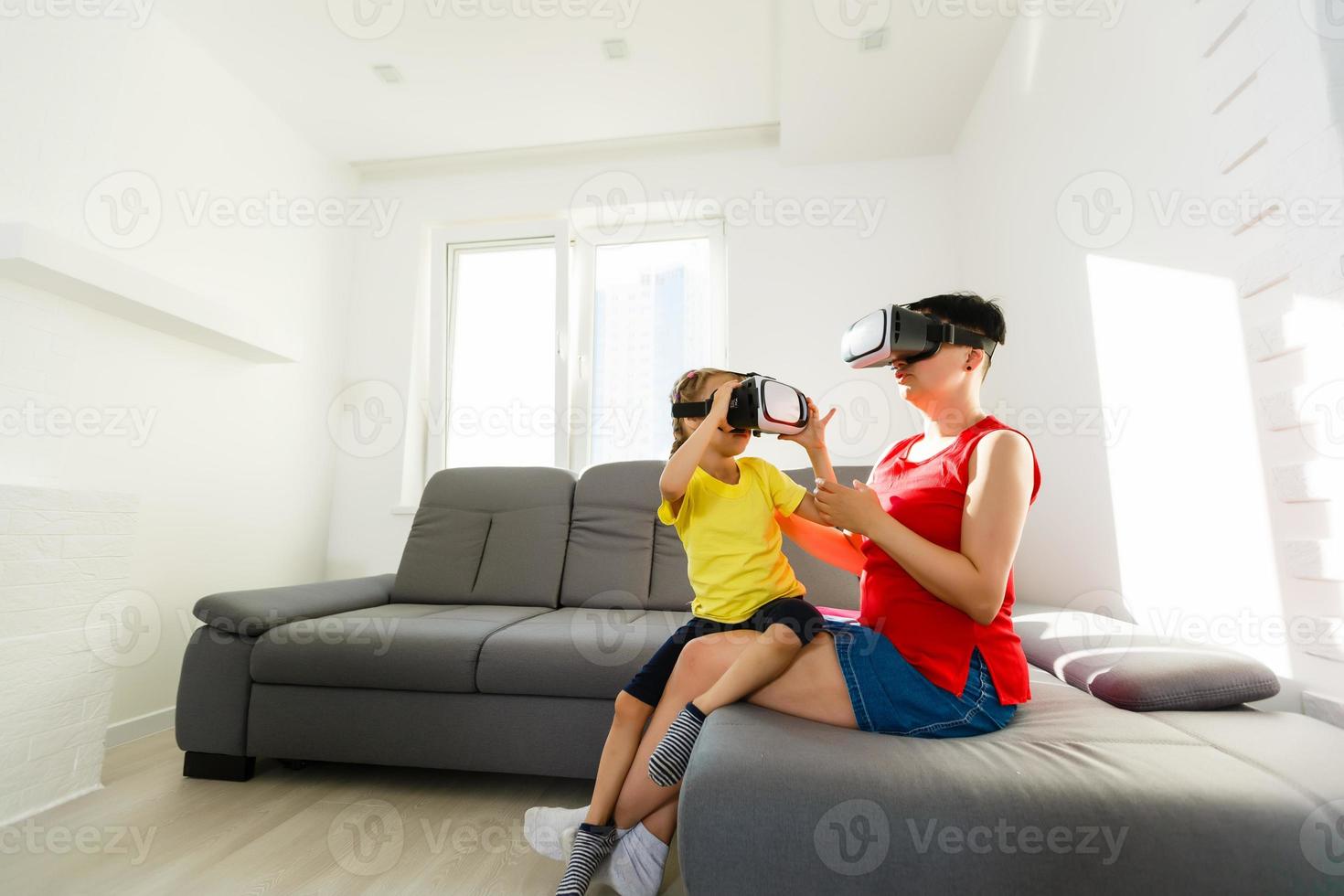 Young woman playing with cute little girl. Watching through VR device. photo