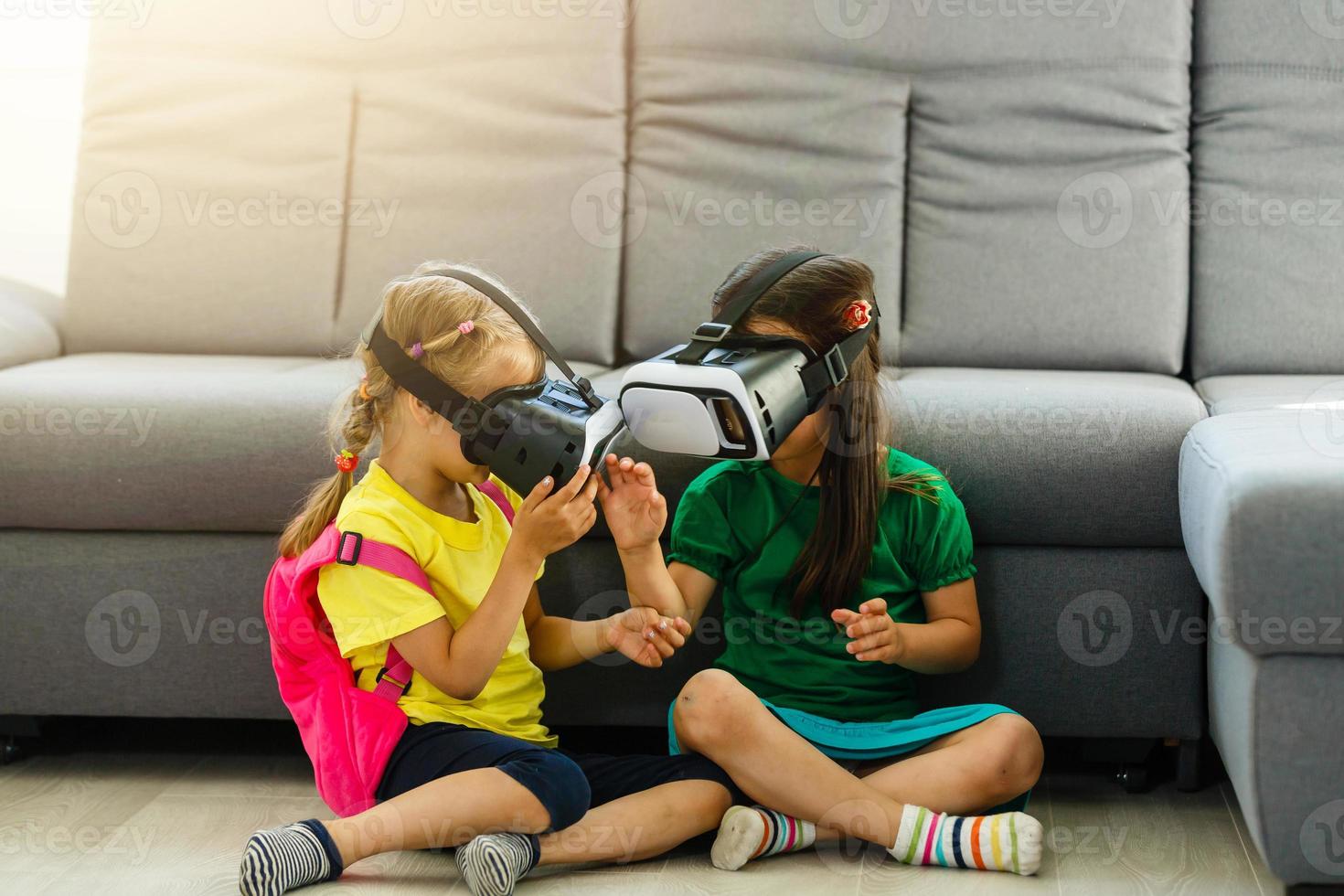 Lifestyle shot of an amazed two little kids using a virtual reality goggles with mouth open shocked seated in the living room at home. family activity concept. photo