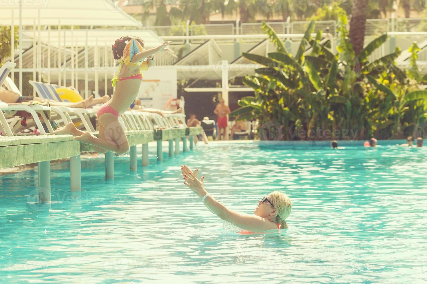 retrato de sonriente hermosa mujer y su pequeño linda hija en Gafas de sol cerca piscina al aire libre foto