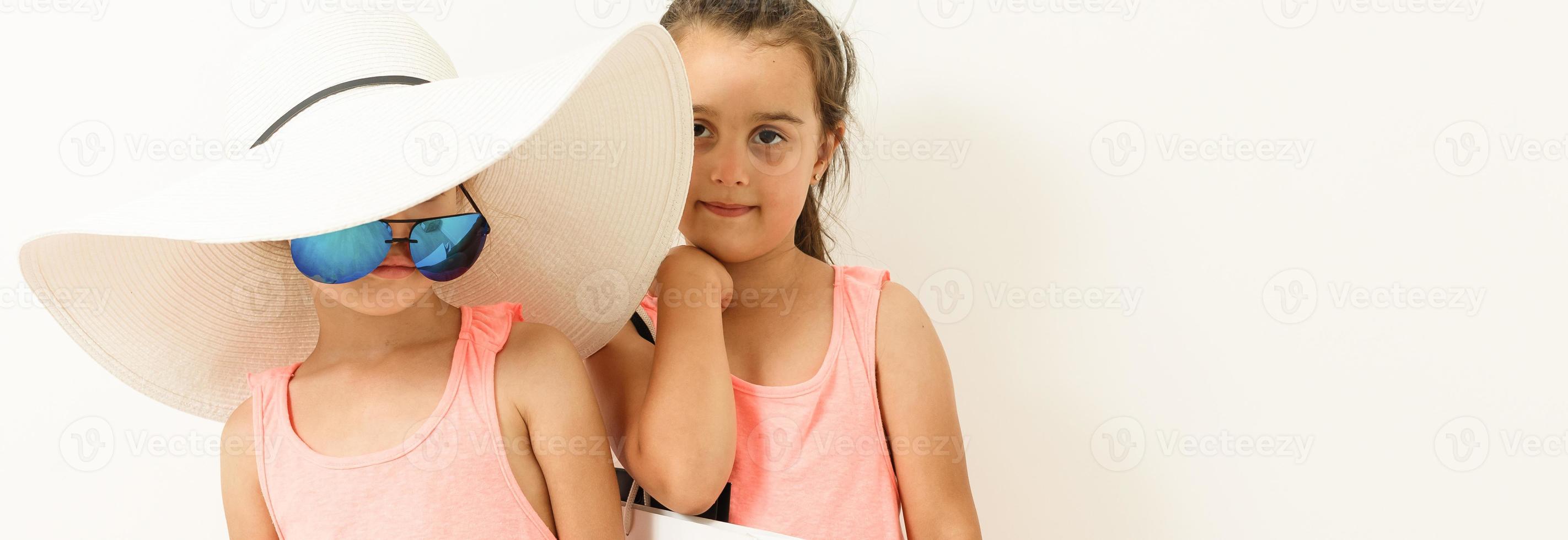 Cute fashion kids are standing together. Little girl in straw hat and striped red dress and little boy in white shirt in the studio on white background. Vacation, friendship, fashion for children photo