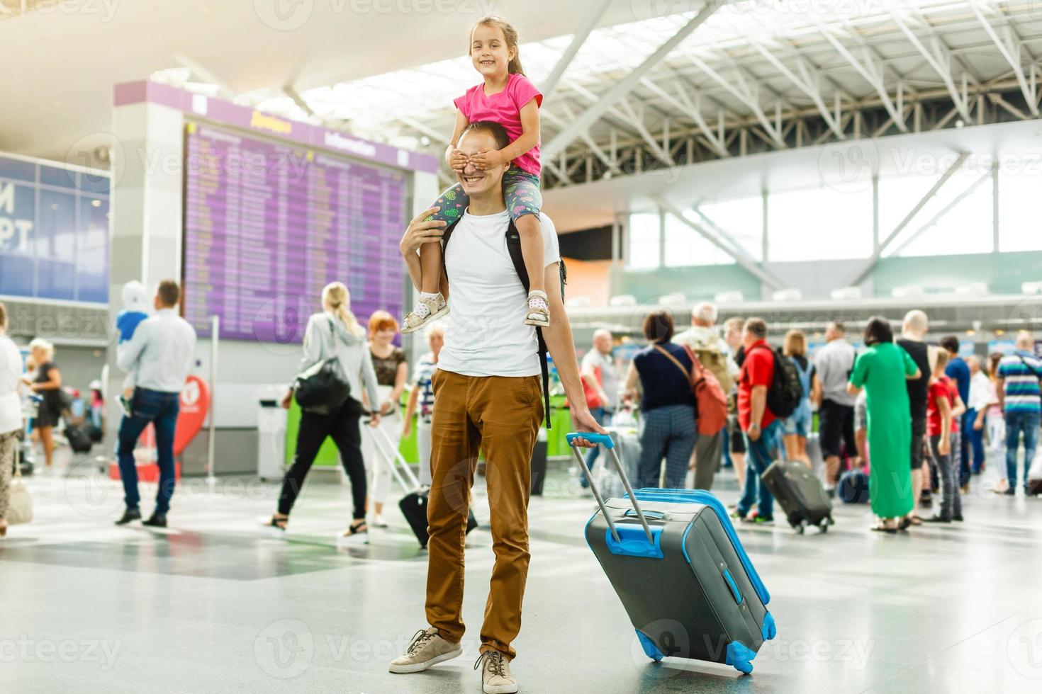 Young father holding little girl on his neck while reading departure information on electronic timetable in airport photo