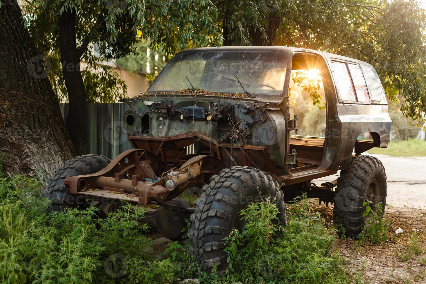 Close-up of an old rusty car with a broken door and no wheels on the background of a green coniferous forest photo