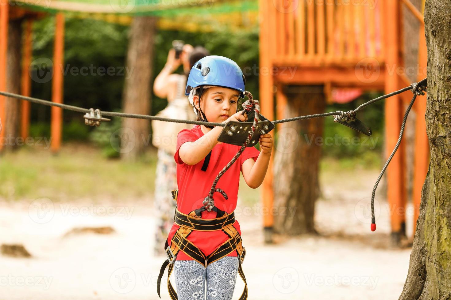 Portrait of cute little girl walk on a rope bridge in an adventure rope park. photo