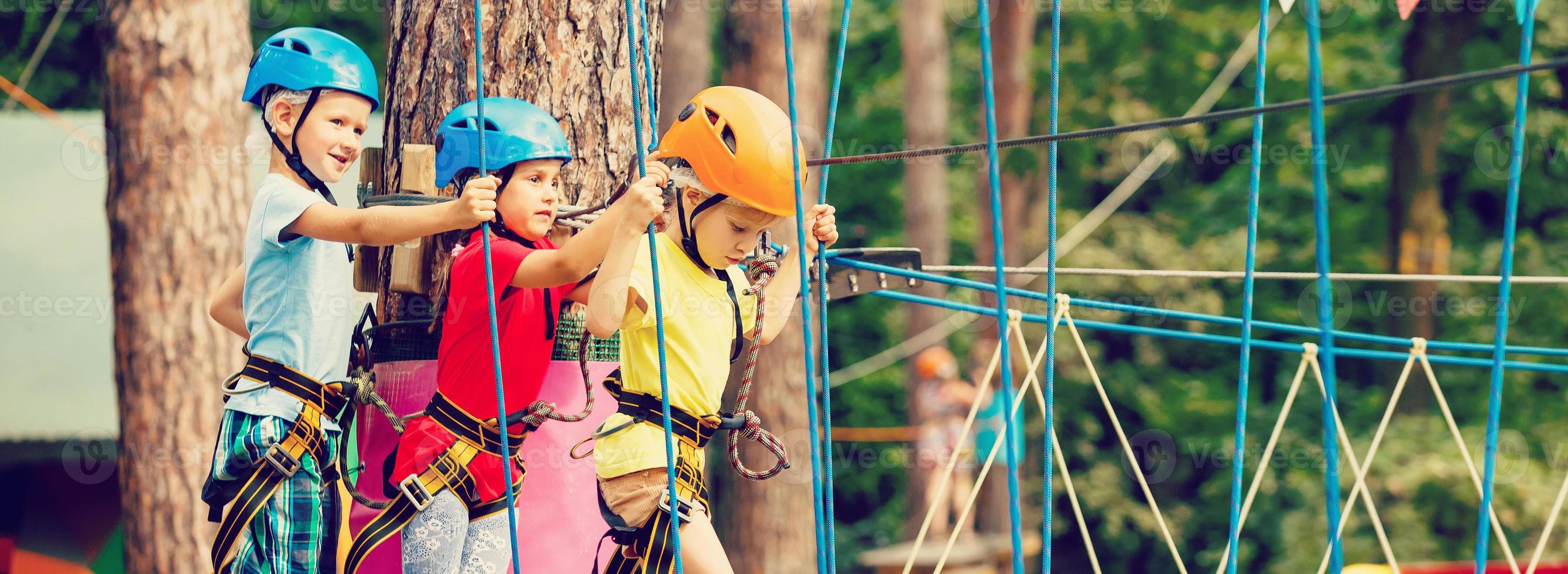 niño en bosque aventuras parque. niños escalada en alto cuerda camino. agilidad y alpinismo al aire libre diversión centrar para niños. pequeño niña jugando al aire libre. colegio yarda patio de recreo con cuerda forma. foto