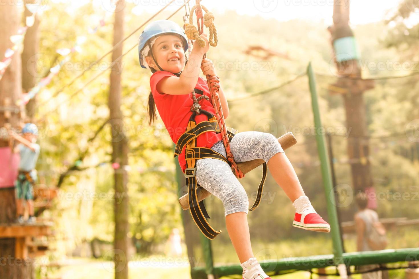 valiente joven niña en casco sube en árbol tapas en diversión cuerda parque en verano vacaciones, niños acampar foto