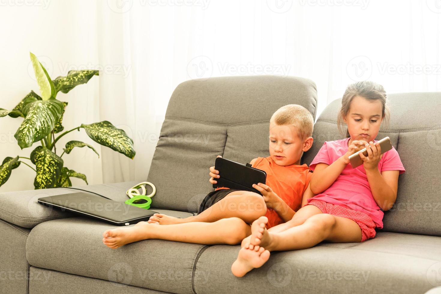 brother and sister sitting on couch at home using mobile phone. Close up surprised daughter and frustrated son looking at device screen. Technology new generation addicted with gadgets concept photo