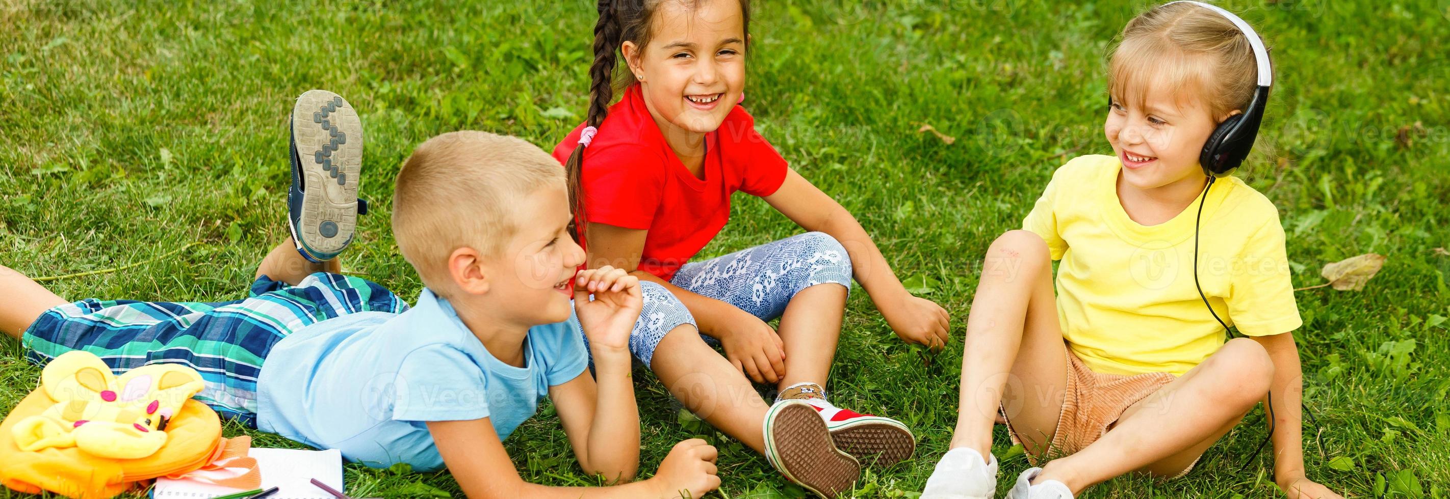 grupo de contento niños jugando al aire libre. niños teniendo divertido en primavera parque. amigos acostado en verde césped. foto