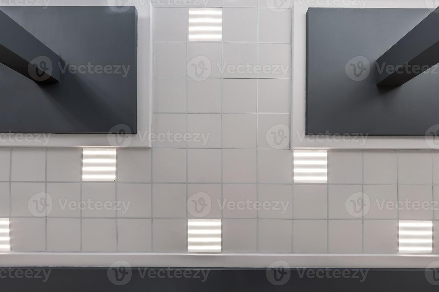 cassette stretched or suspended ceiling with square halogen spots lamps and drywall construction in empty room in house or office with column. Looking up view photo
