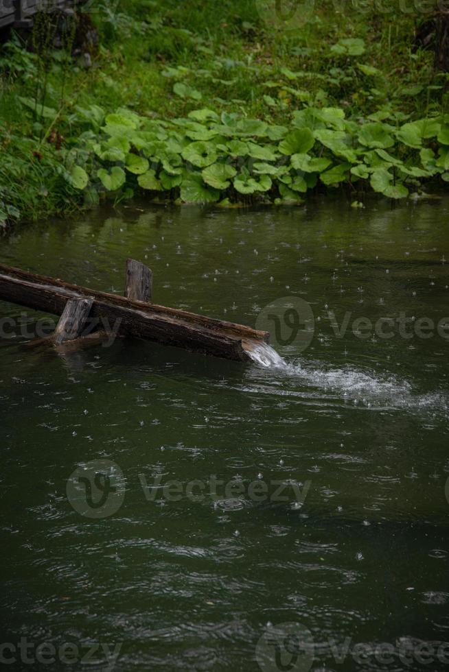 A pond in which there is a small wooden channel where water flows through photo