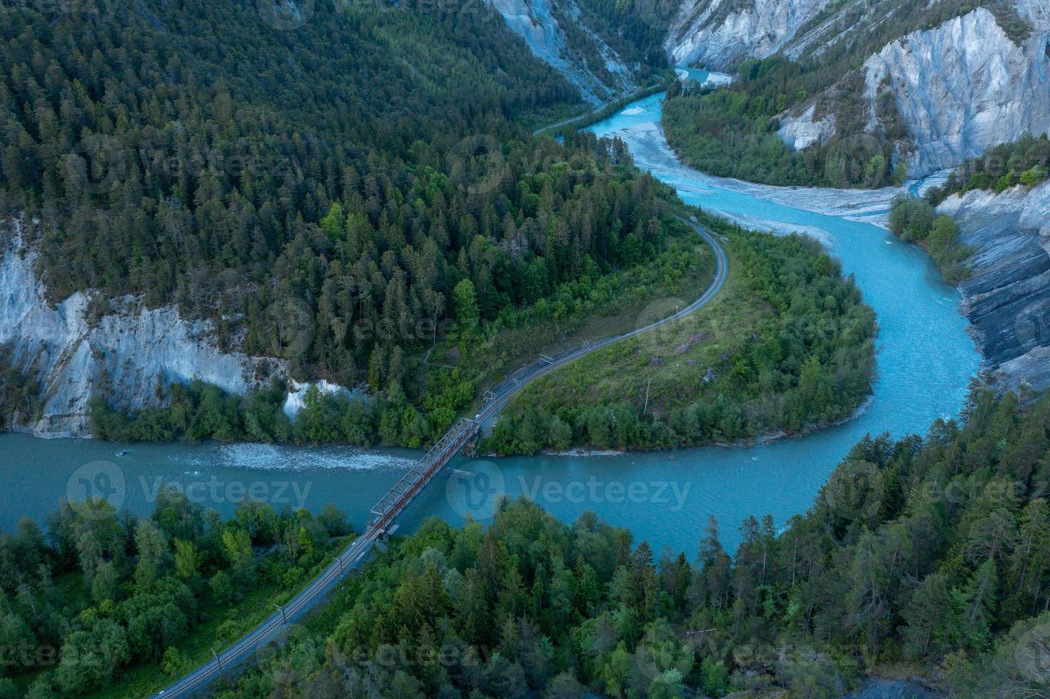 A river that runs in a S curve between the mountains,a railroad bridge crosses the river photo