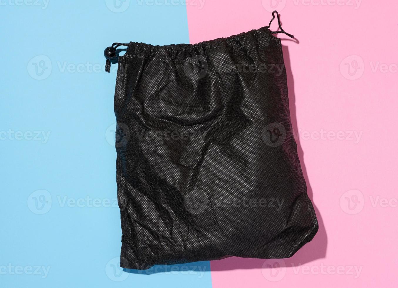 Black textile bag with a rope on a blue pink isolated background, photo