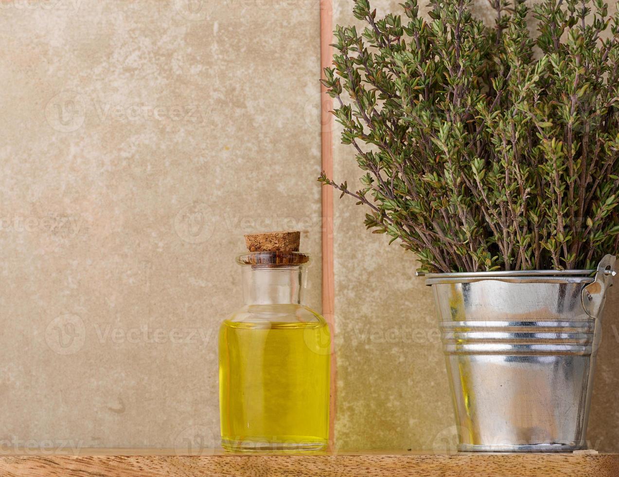 A clear glass bottle with oil and fresh thyme branches in a miniature bucket on a wooden table, cosmetic procedure oil. photo