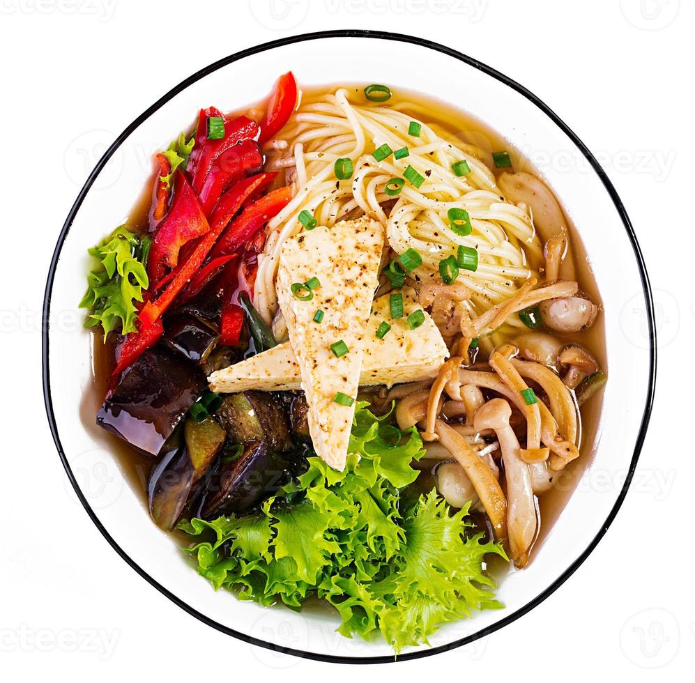 Asian vegan noodles soup with tofu cheese, shimeji mushrooms and fried eggplant in bowl on white background. Top view photo