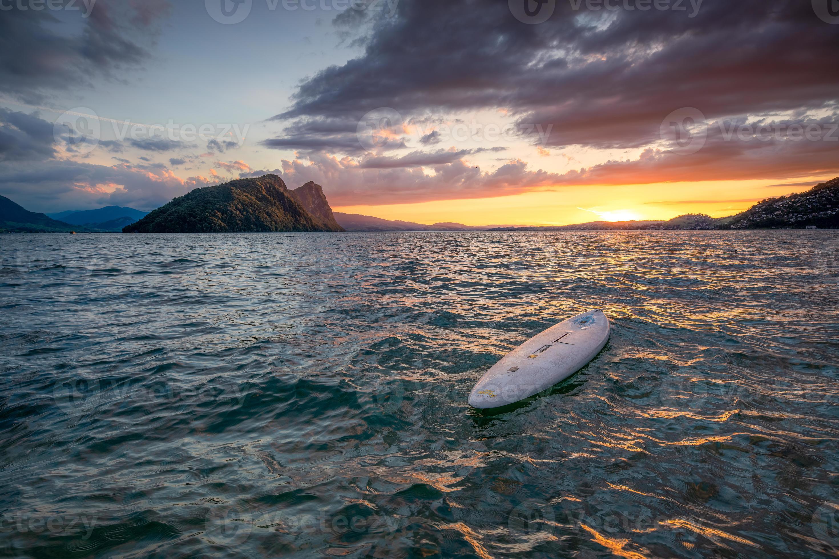 A surfboard lies in the water in a beautiful landscape while the sun