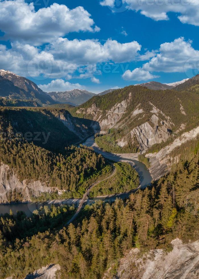 A river that runs in a S curve between the mountains,a railroad bridge crosses the river photo