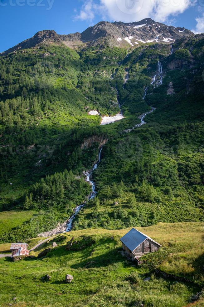 A waterfall running down the mountain in the valley is a small hut photo