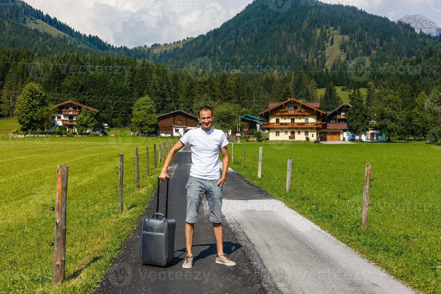 Traveler man walking with suitcase in the street in the mountains. Travel concept. photo