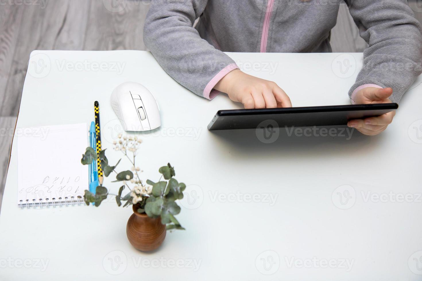 tablet in the hands of a child sitting at a white table, copy space, online learning photo