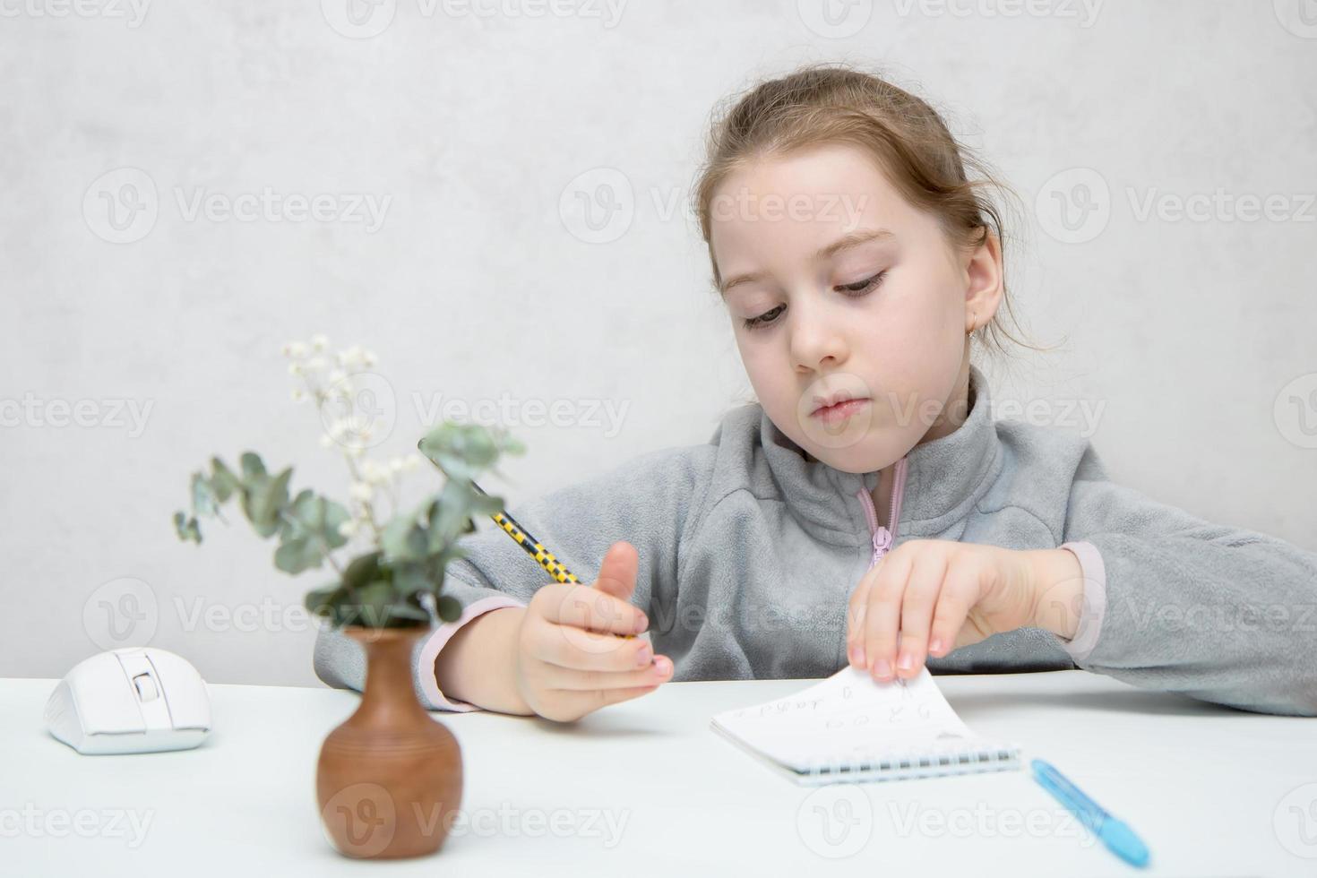 little cute girl writes intently in a notebook at the table photo