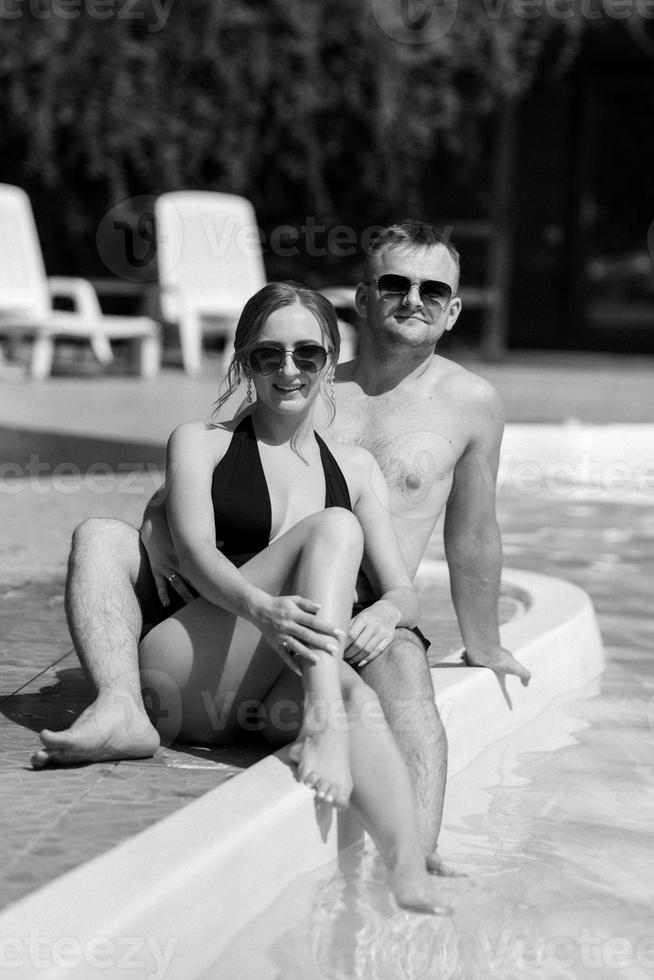 guy and a girl in bathing suits are relaxing, near the blue pool photo