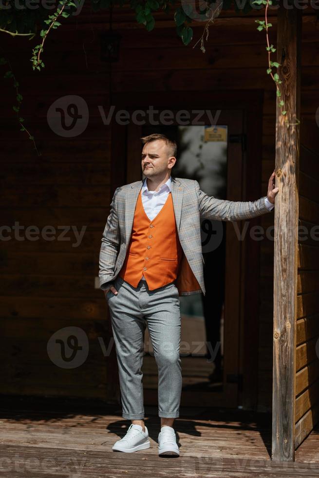 portrait of the groom in a gray suit and an orange vest photo