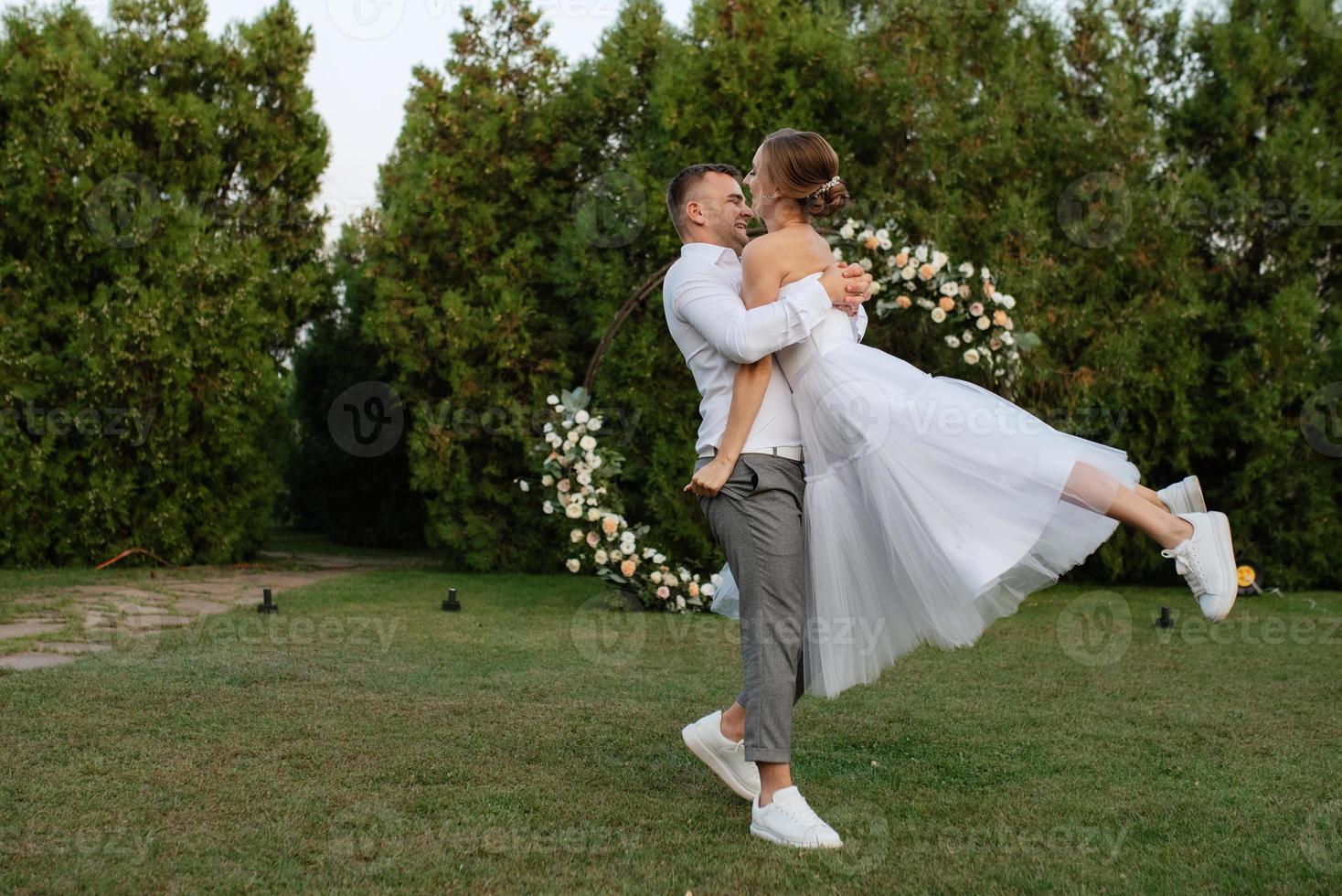 the first dance of the groom and bride in a short wedding dress on a green meadow photo