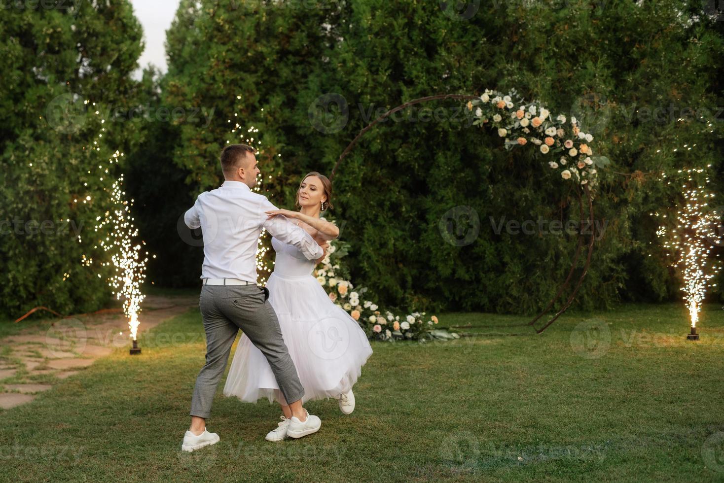 the first dance of the groom and bride in a short wedding dress on a green meadow photo