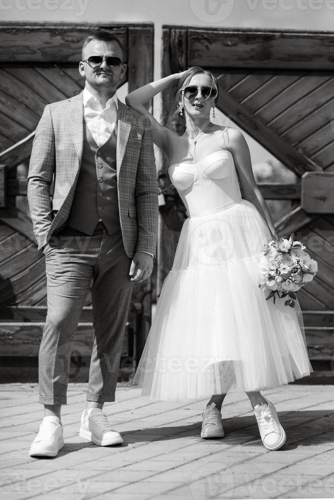 young couple bride in a white short dress and groom in a gray suit near the wooden gate photo