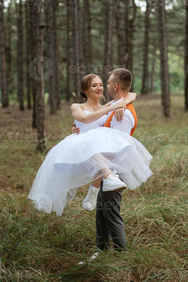 young couple bride in a white short dress and groom in a gray suit in a pine forest photo