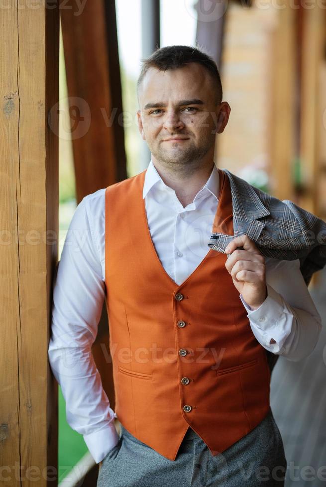 portrait of the groom in a gray suit and an orange vest photo