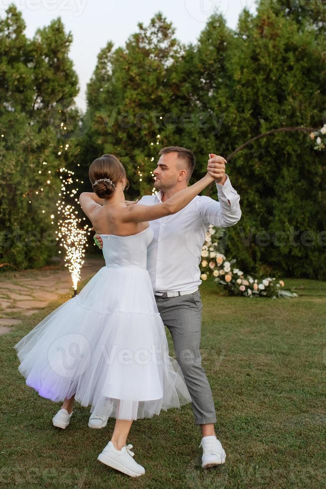 the first dance of the groom and bride in a short wedding dress on a green meadow photo