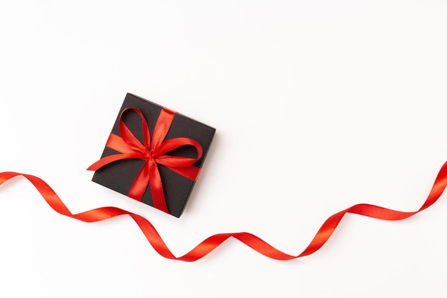 Flat lay of black present box with red bow and ribbon on the white background photo