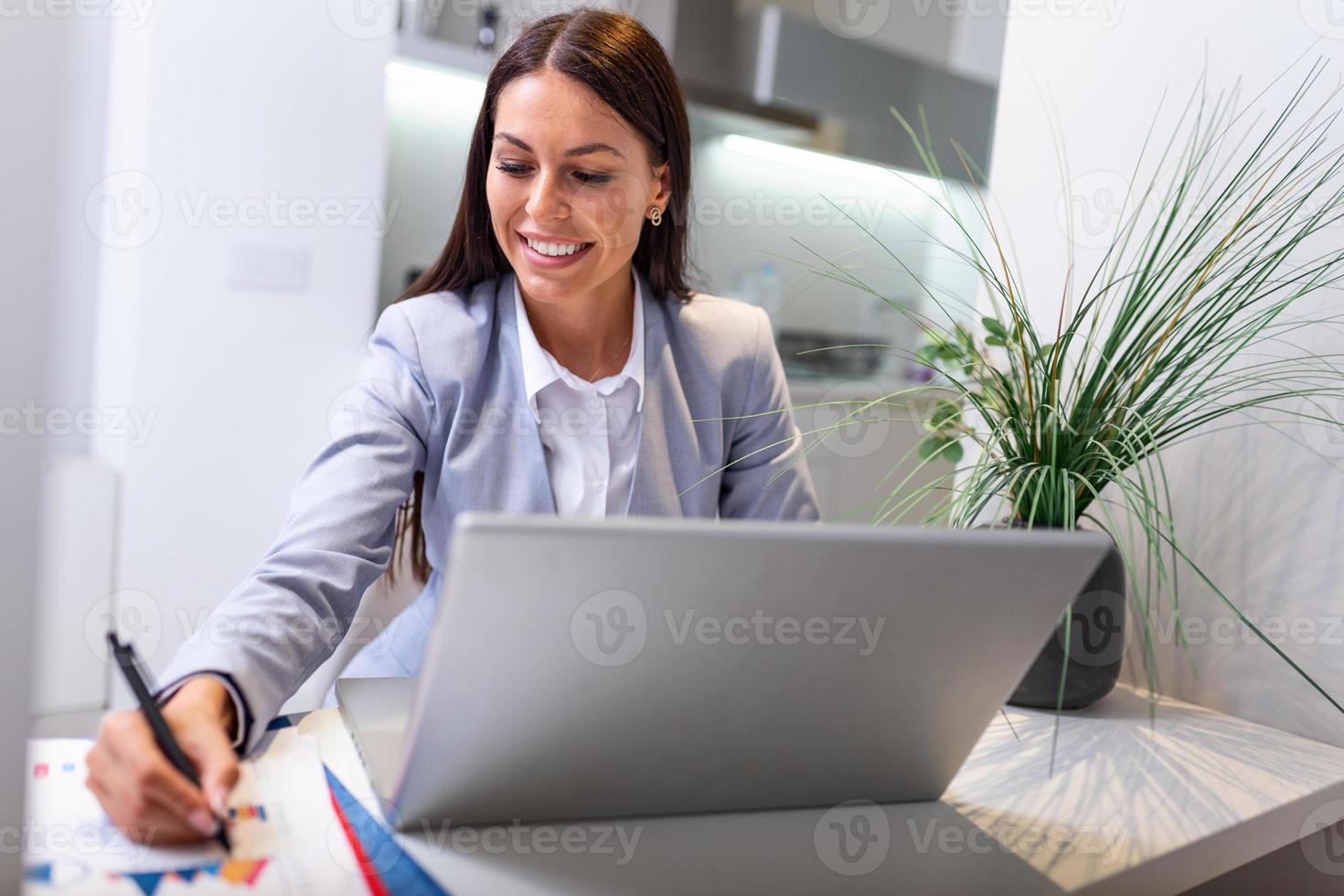 People study online course via internet. Young woman watching business lesson from laptop computer and note lecture to notebook at home. photo