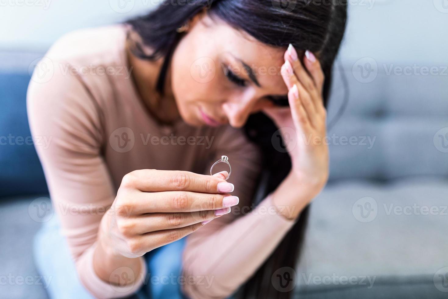 Upset woman holding wedding ring close up cropped image, took off jewellery demonstrate show it as symbol of divorce family split break up, legally dissolve wifehood with husband, bustup of a marriage photo