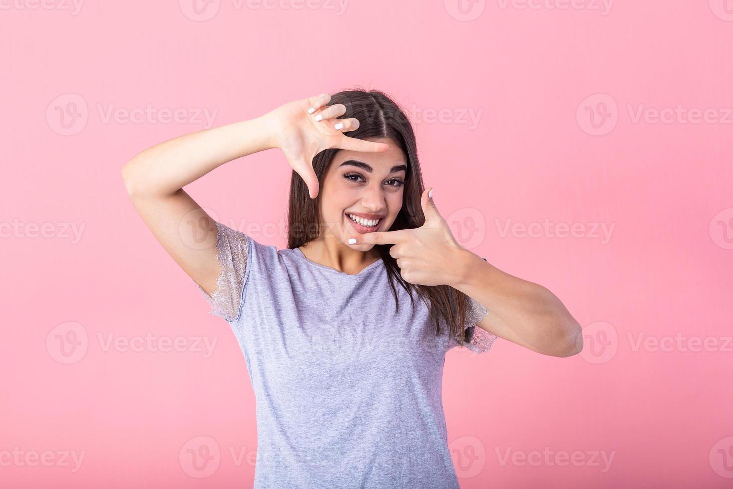 Happy young woman making frame gesture with fingers over pink background. Portrait of a happy smiling woman framing her face with her hands isolated photo