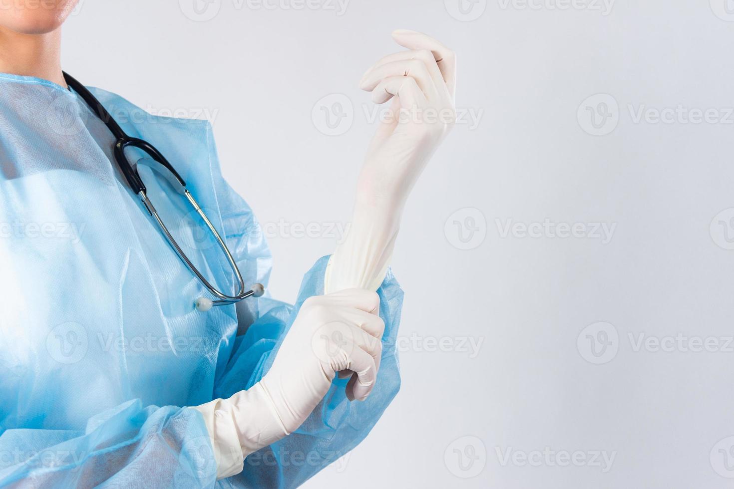Female doctor surgeon preparing for the surgical operation, she is wearing gloves and scrubs, healthcare and preparation concept. Young doctor putting on rubber gloves in clinic close up photo