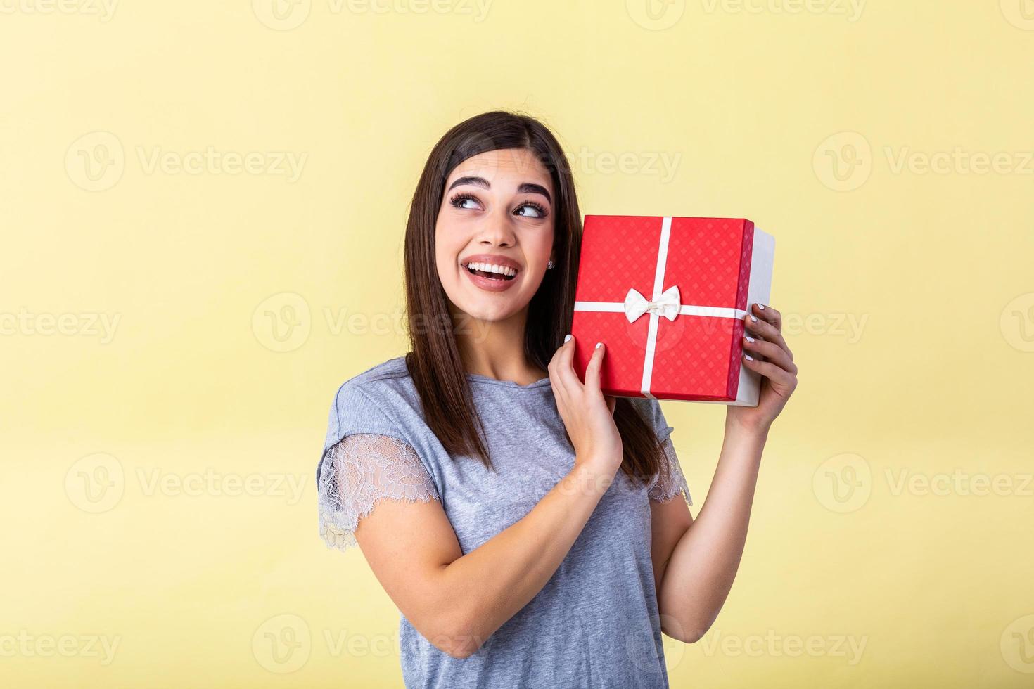 Portrait of young lovely nice sweet glamorous girl lady, wearing gray top, carrying gift box, wondering about surprise. Isolated over bright vivid yellow background photo